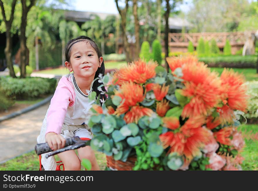 Cute little Asian girl riding on bicycle with basket of flower at the garden.
