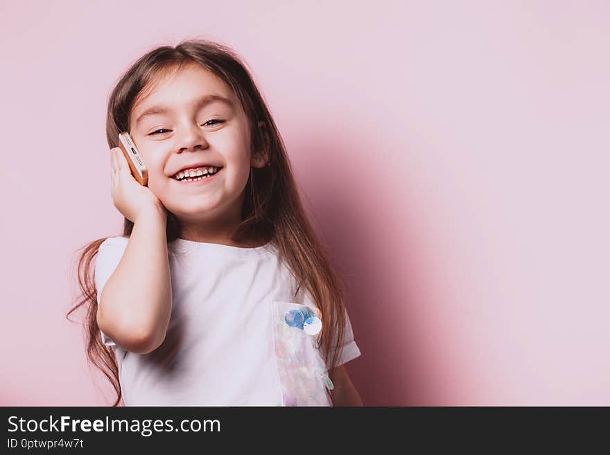 Cute little happy girl talking on phone on pink background