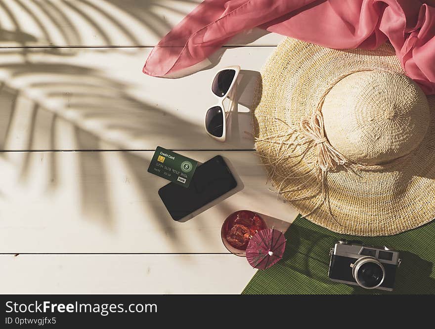 Summer beach vacations and tropical destinations: straw hat, sunglasses, credit card, smartphone and tropical foliage shadow