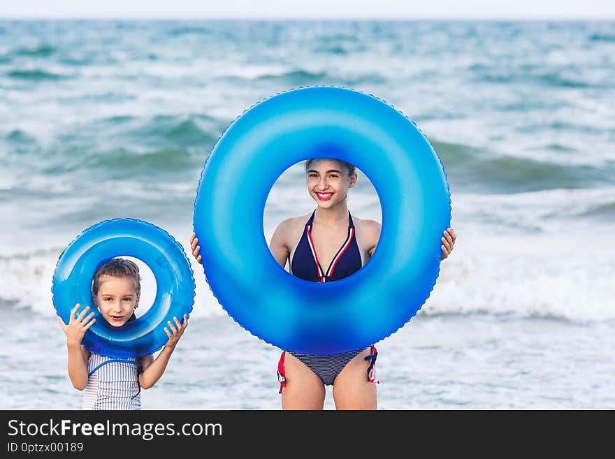 Happy girls hold floating inflatable circles on sea beach.