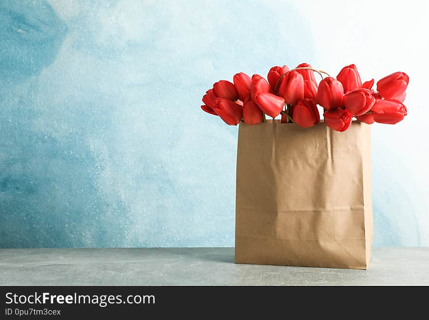 Paper bag with beautiful red tulips on table against blue background