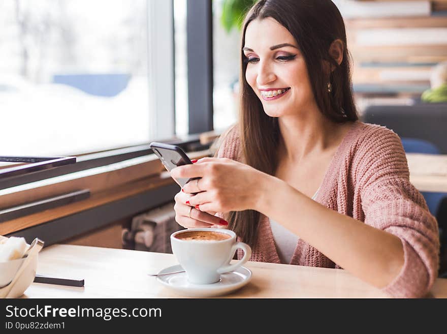 Beautiful Young Woman Sits At A Table In A Cafe With A Cup Of Coffee And Uses The Phone