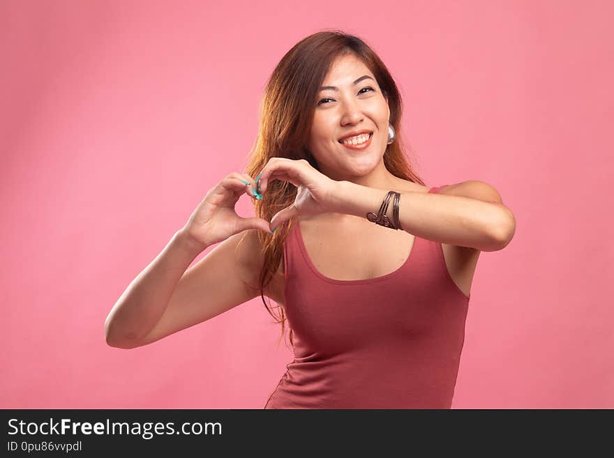 Young Asian woman show heart hand sign on pink background