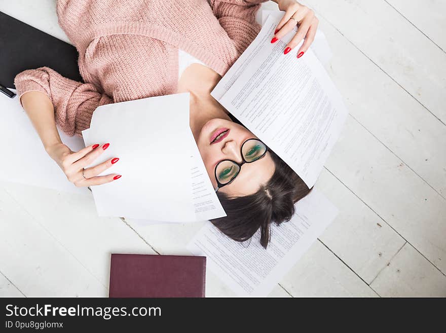 A beautiful woman in stylish glasses lies on the floor among the papers and documents, the girl freelancer smiles and