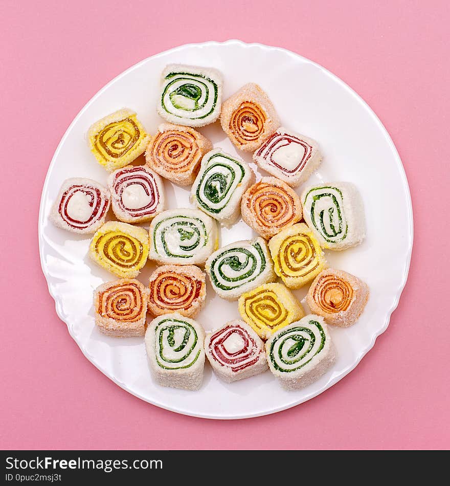 Turkish sweets of different colors on a white plate on pink background