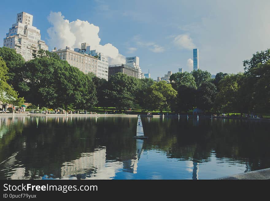 A Reflecting Lake In A Park With Tall Buildings And Beautiful Sky