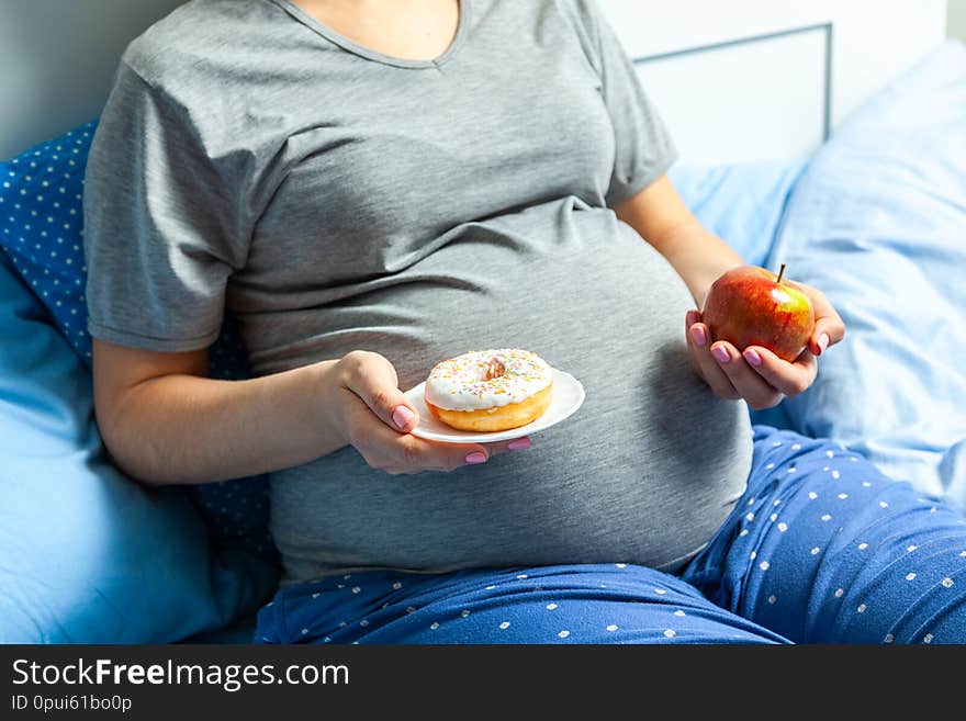 Pregnant Woman With Stomach And Holding An Apple And Donut. Diet For Pregnant Women.