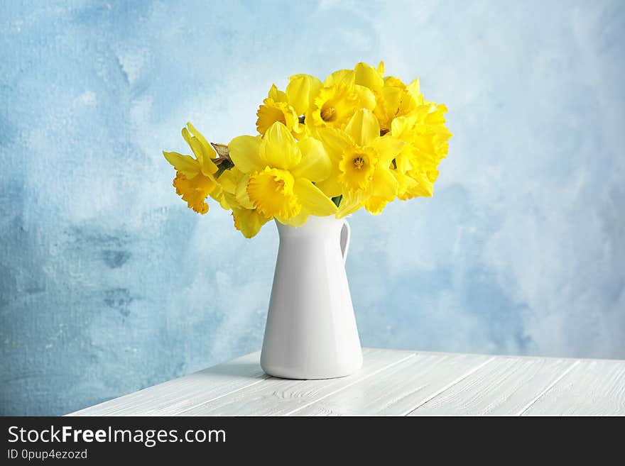 Bouquet of daffodils in jug on table against color background. Fresh spring flowers