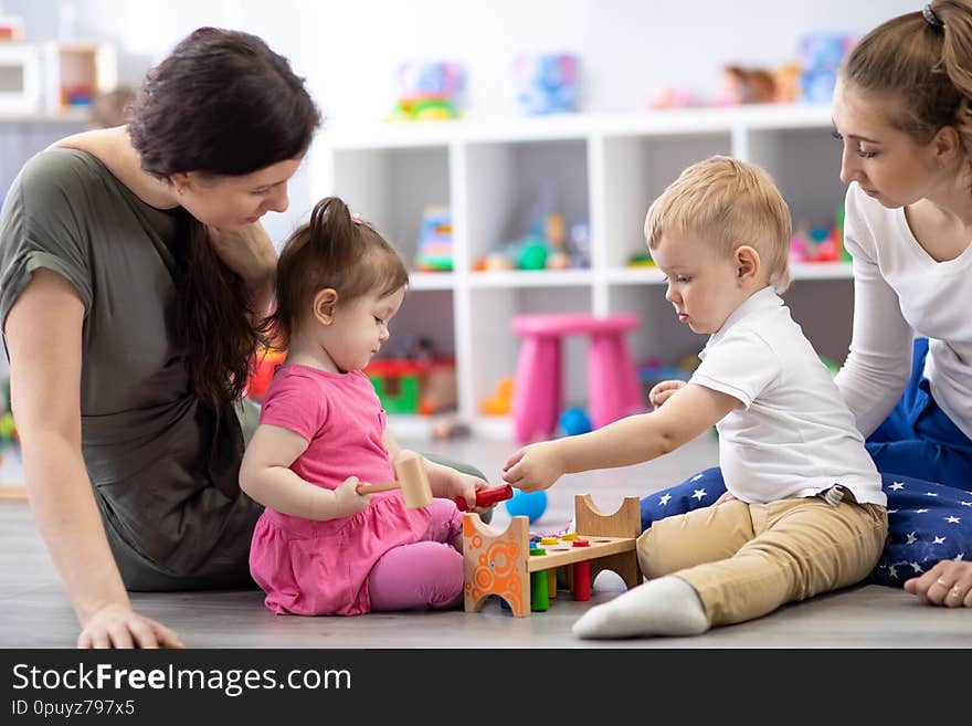 Group of babies playing together with mothers in the classroom in nursery or preschool