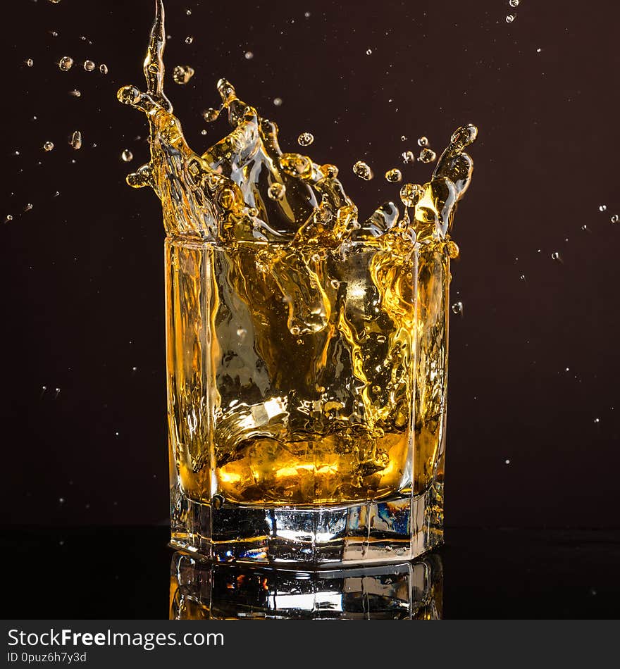 Hexagonal glass of whiskey with ice and splashes from an abandoned and falling ice cube