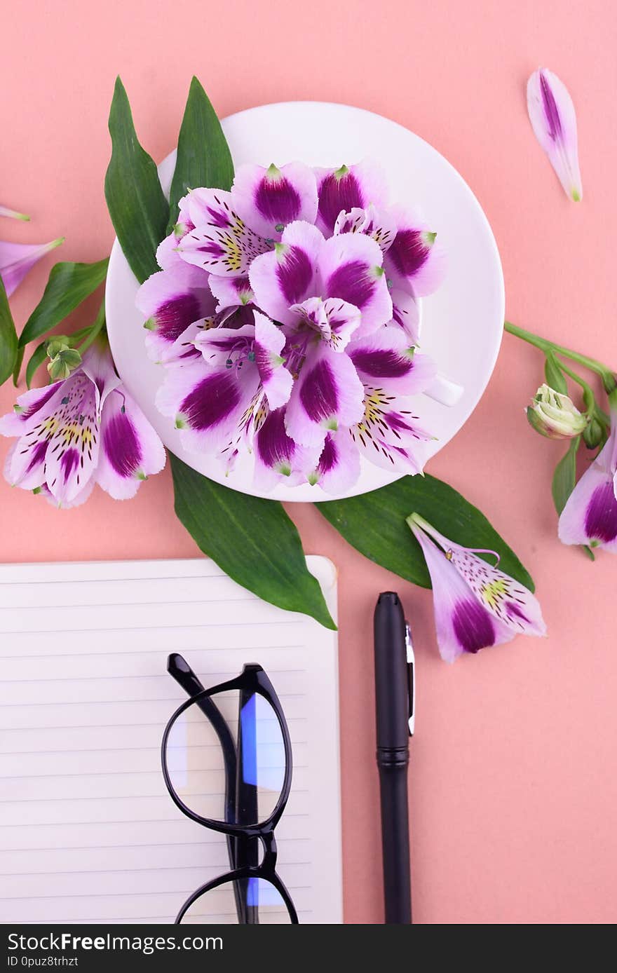 Fragrant Tea In A White Cup, Beautiful Flowers, A Pink Background, A Notebook With A Pen And Glasses