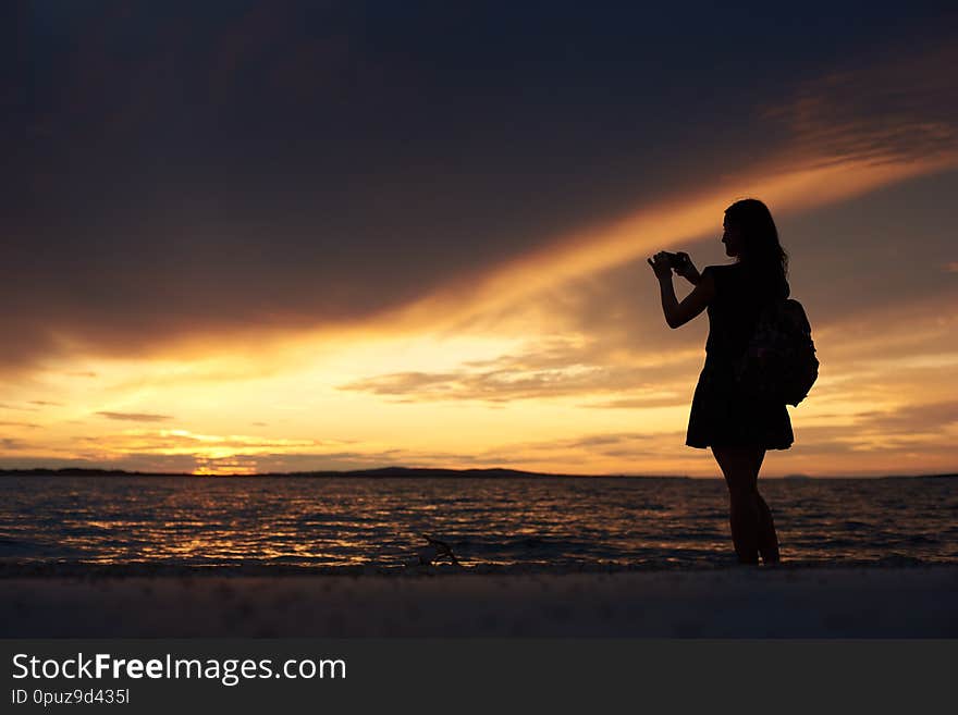 Silhouette of woman alone at water edge, enjoying beautiful seascape at sunset.