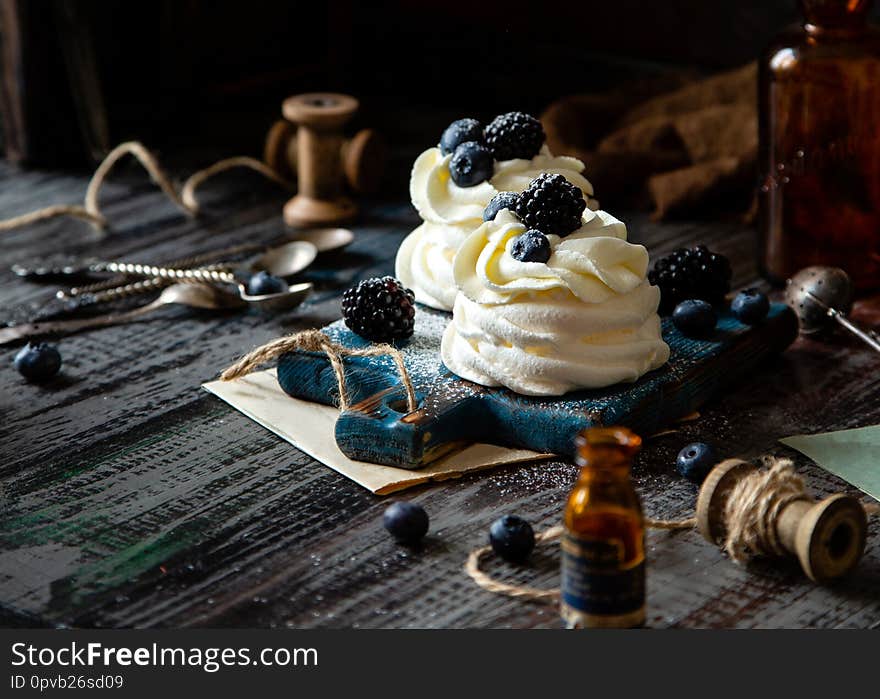 Two homemade white mini desserts pavlova on wooden blue board with whipped cream and blueberries, blackberries on rustic table