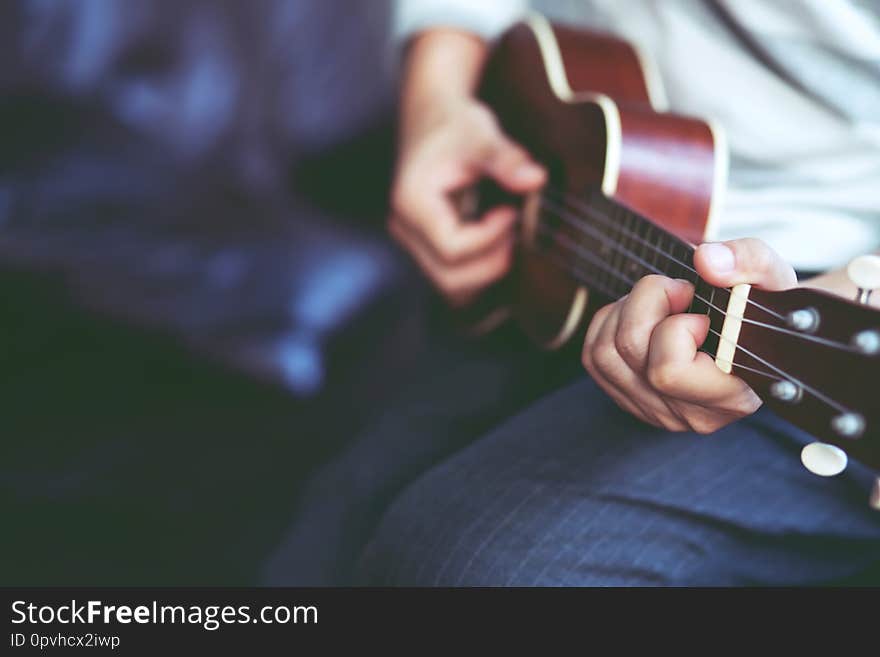 Closeup of young man hands playing acoustic guitar ukulele at the sofa sit Enjoy living room. Closeup of young man hands playing acoustic guitar ukulele at the sofa sit Enjoy living room.