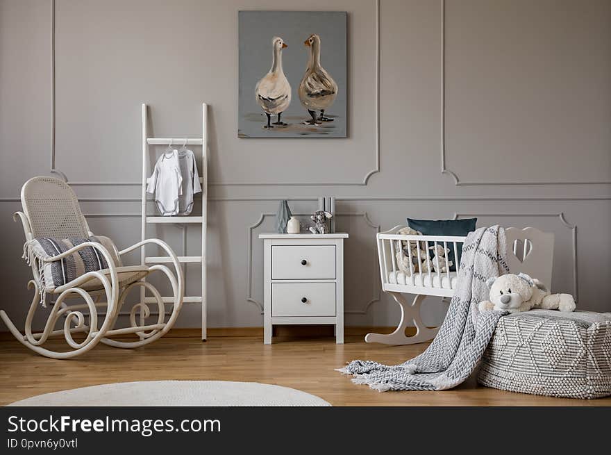 White wooden rocking chair with pillow next to scandinavian ladder, chest of drawers and cradle, copy space on wall with cute