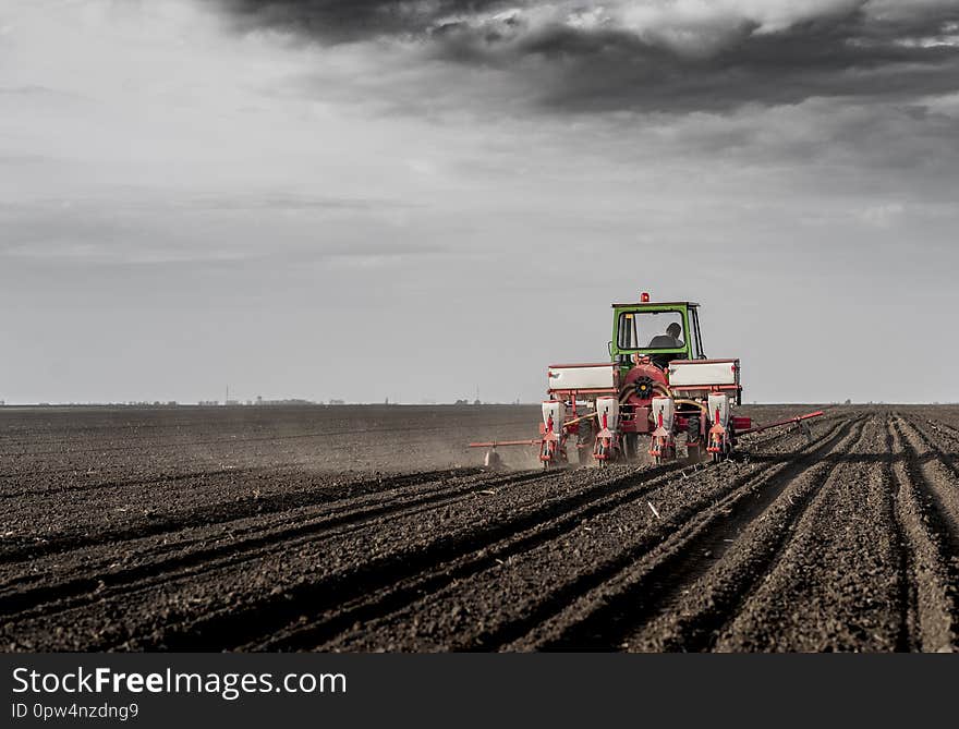 Farmer with tractor seeding - sowing crops at agricultural fields in spring