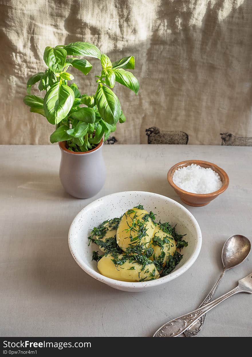 BoBoiled potatoes fried with butter and aromatic herbs in a white plate, gray ceramic pot with growing basililed karshoshka fried with butter and aromatic herbs