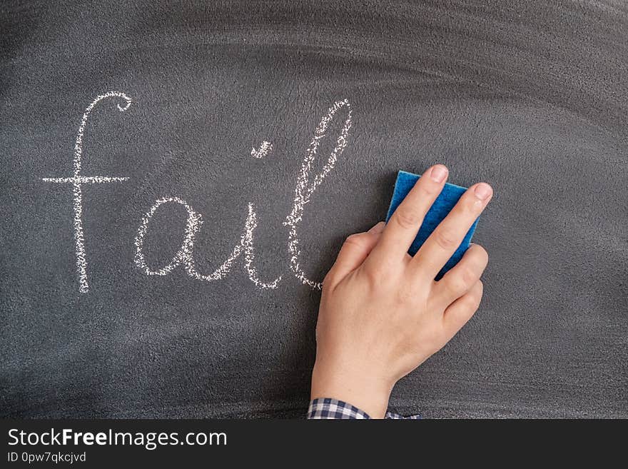 A woman`s hand with a sponge erases the chalk-written word fail from the blackboard. the concept of success, forget failure