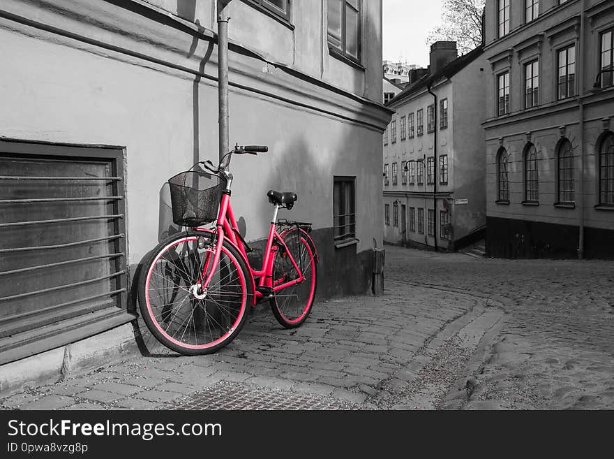 A picture of a lonely red bike standing in the typical street in Stockholm. The bike looks to be modern in a retro style. The background is black and white.