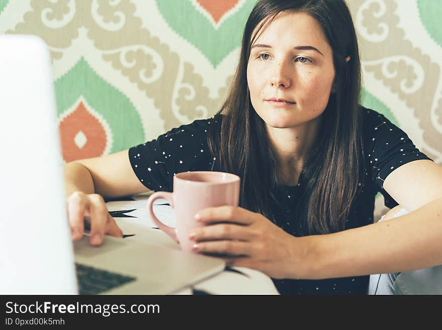 Female freelancer looks at a laptop monitor and holds a cup of coffee, business concept. Female freelancer looks at a laptop monitor and holds a cup of coffee, business concept