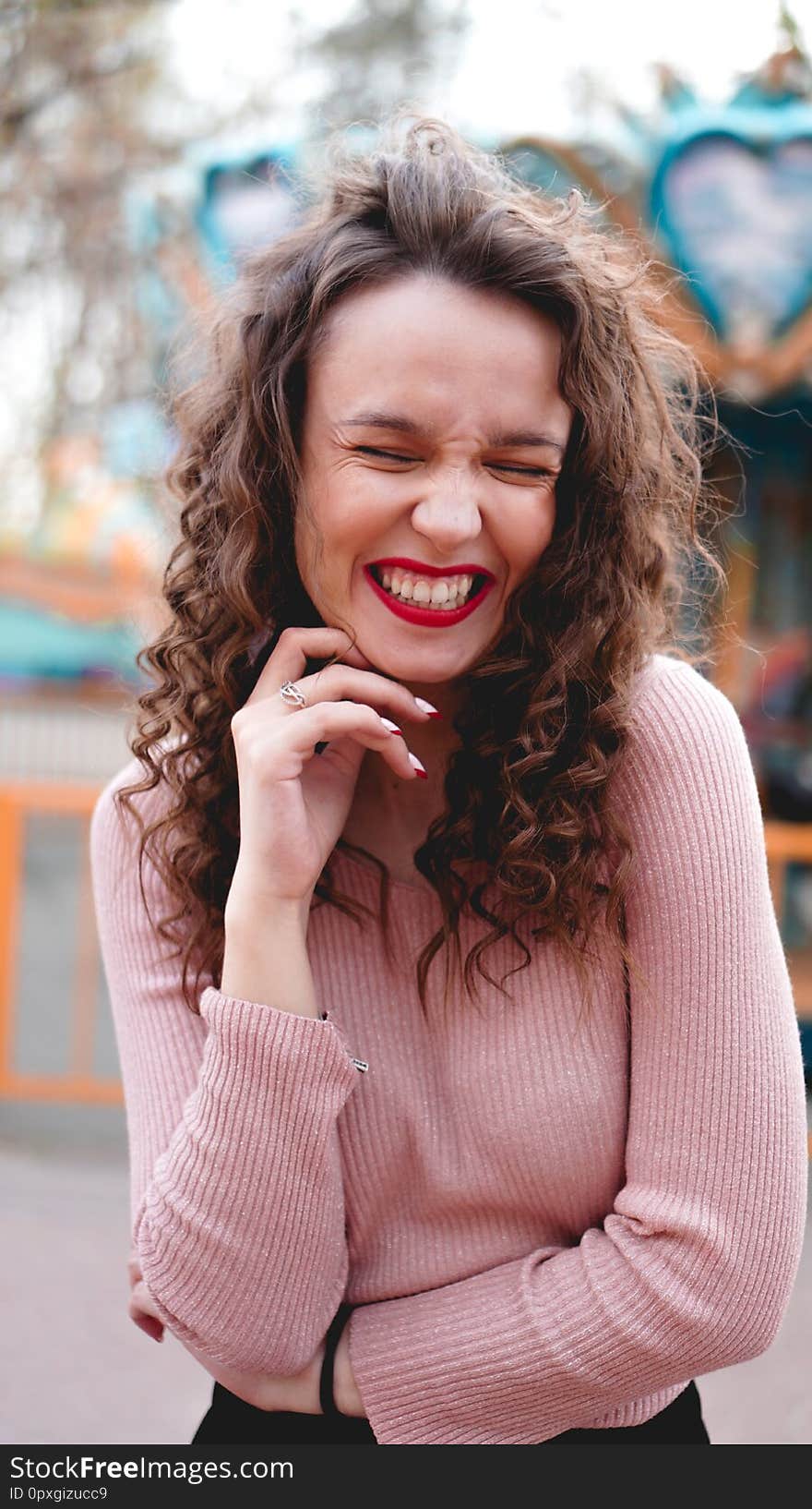 Girl chilling in amusement park in weekend morning. Laughing good-humoured female model with curly hair standing near carousel. Girl chilling in amusement park in weekend morning. Laughing good-humoured female model with curly hair standing near carousel.