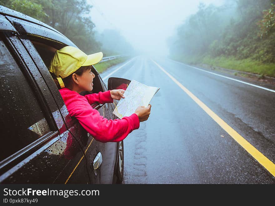 Asian Women Travel Relax In The Holiday. Traveling By Car Park. View Map For Nature Tours During The Rainy Season