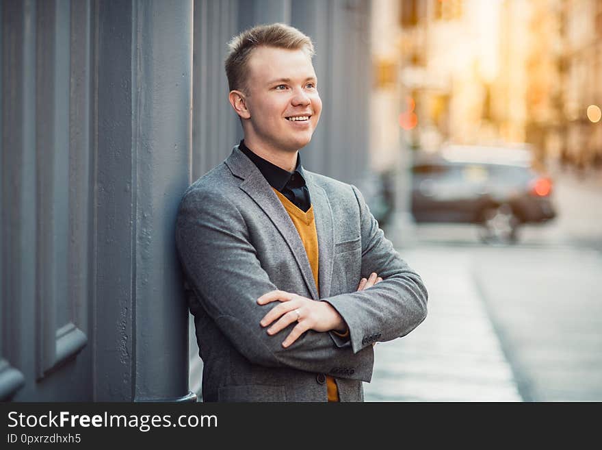 Handsome smiling young adult businessman standing outdoors  near wall on city street