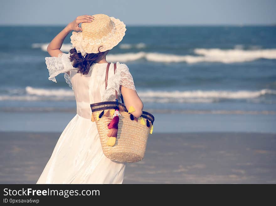 Woman carry big handcraft bag wearing beautiful hat standing and looking to sea with wave and background. Woman carry big handcraft bag wearing beautiful hat standing and looking to sea with wave and background