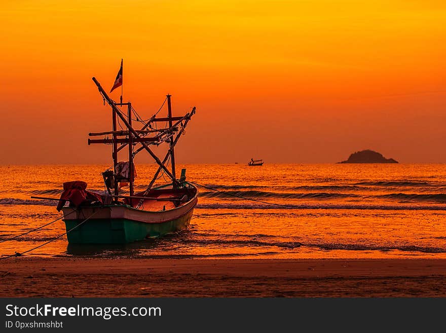 Native Thai style fishery boat anchored on beach in the morning light with island  and colorful sky in background