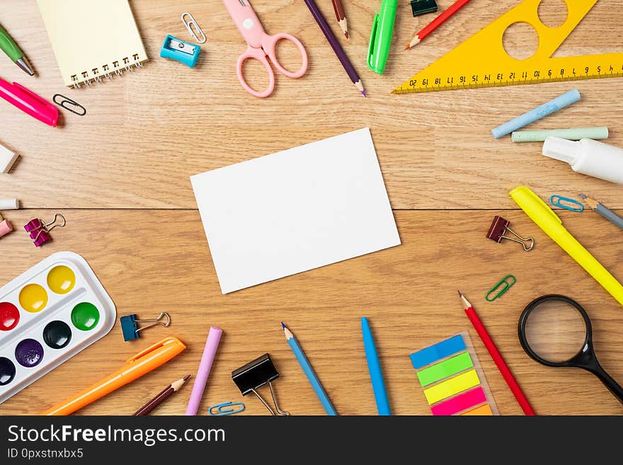 School supplies on wooden table, background with frame made of stationery and blank paper card in center. Education, studying and back to school concept. Child desk top view, copy space, flat lay