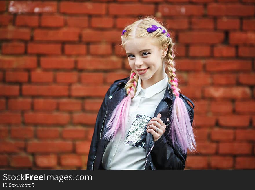 Close up portrait of little beautiful stylish kid girl near red brick wall as background.