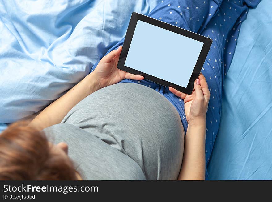 Pregnant woman with belly holds tablet in hands.