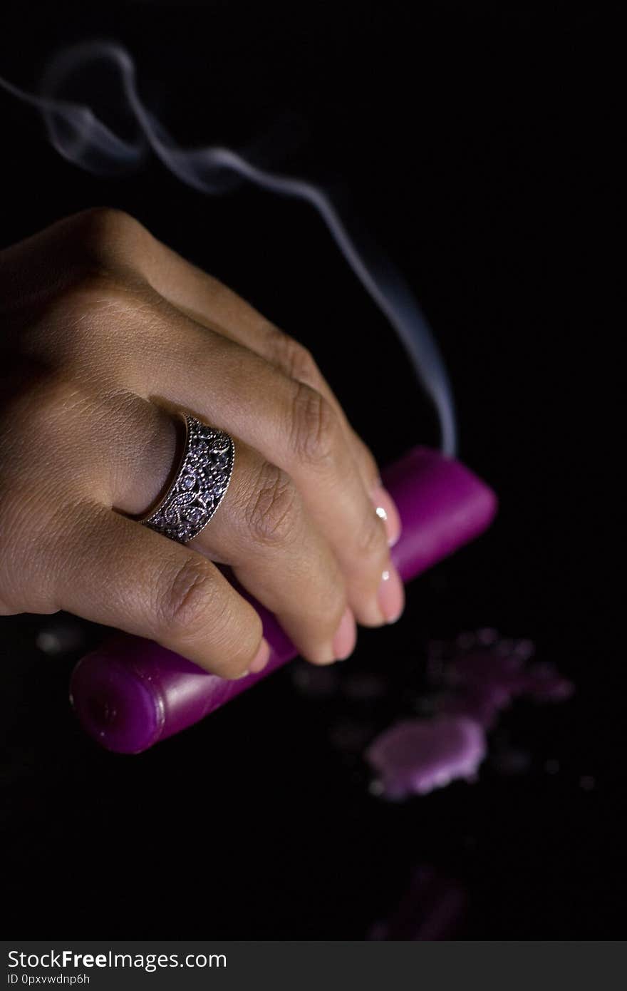 A woman`s hand with a beautiful silver ring holds a smoking purple candle.
