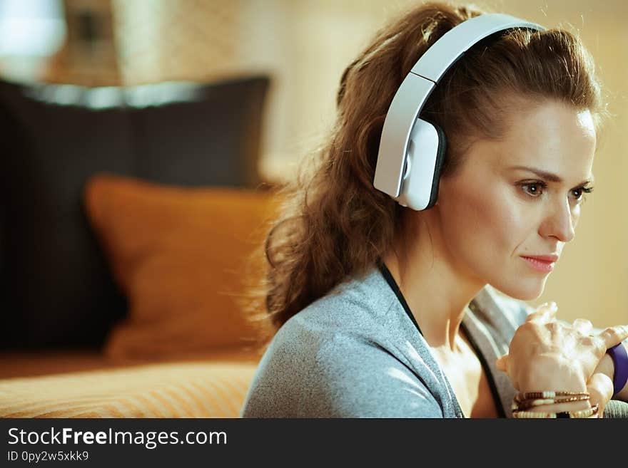 Portrait of pensive active woman in sport clothes listening to the music with headphones in the modern house. Portrait of pensive active woman in sport clothes listening to the music with headphones in the modern house
