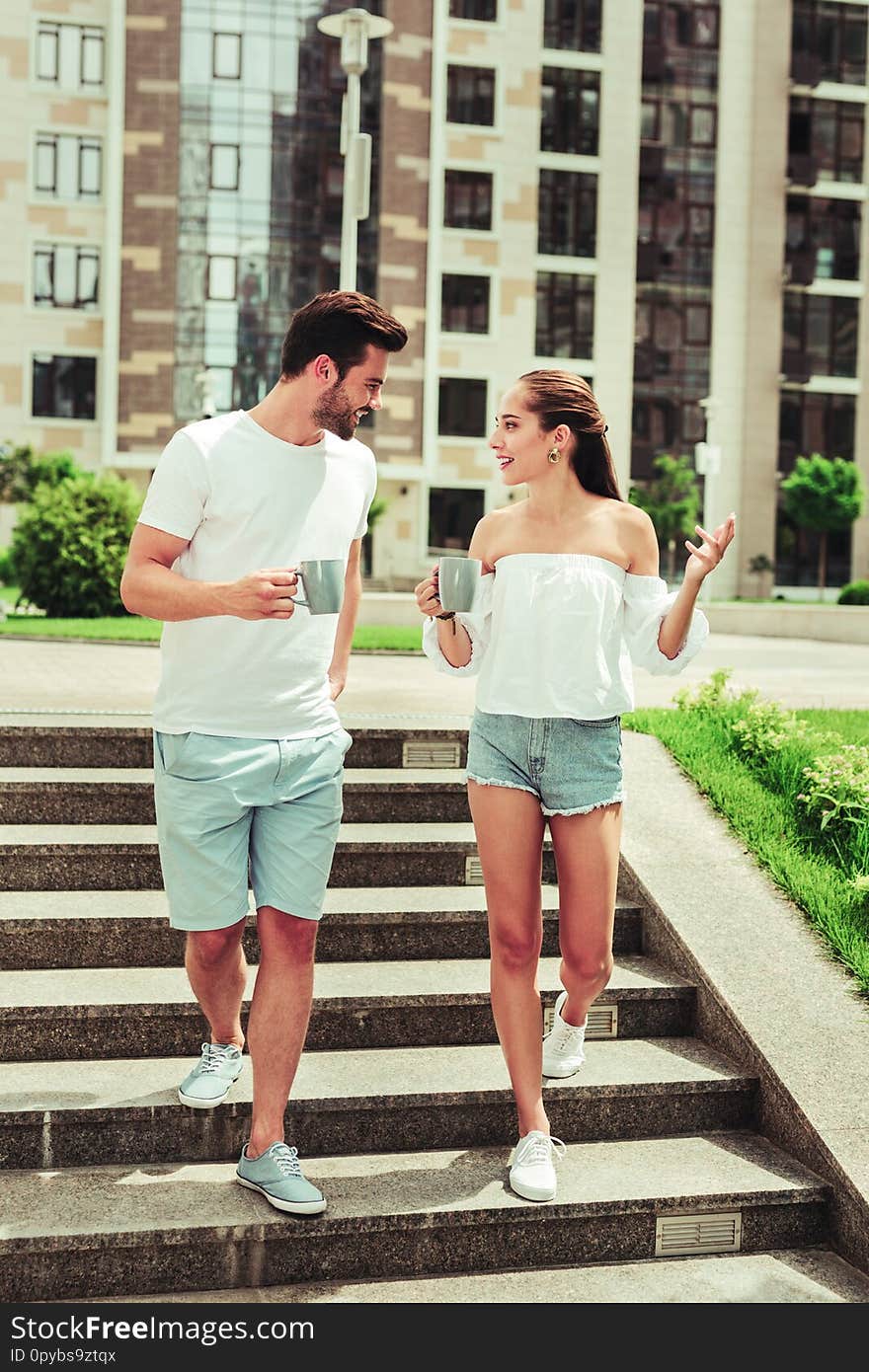 Sporty couple. Amazing longhaired girl holding cup in right hand and looking at new house. Sporty couple. Amazing longhaired girl holding cup in right hand and looking at new house