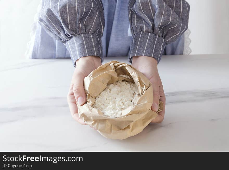 Paper bag with white flour. Woman standing next to the kitchen table and holding paper bag, flour in it