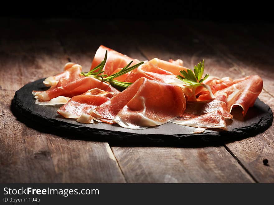 Italian prosciutto crudo or jamon with rosemary. Raw ham on wooden board