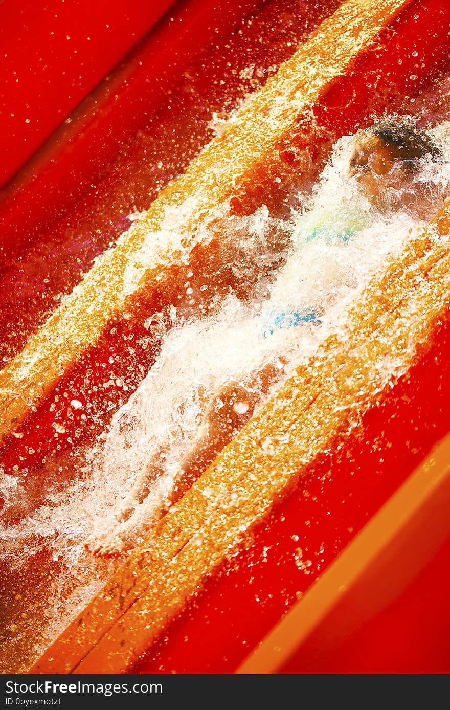 Little caucasian girl inside water splash on waterslide of water park. Summer sunny day.
