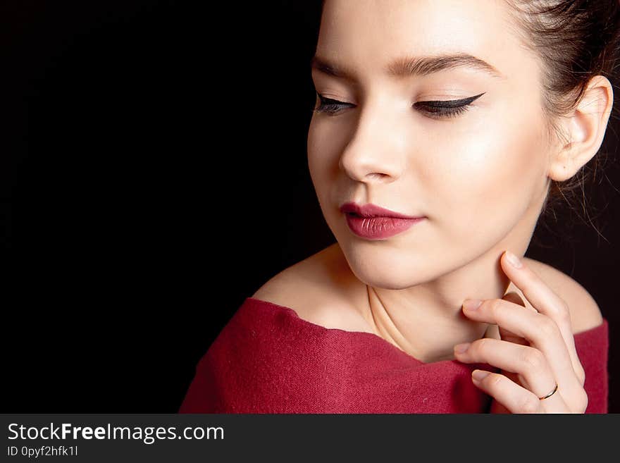 Close-up portrait of a woman with classic make-up with a black arrow and bare lip over her shoulders on a black