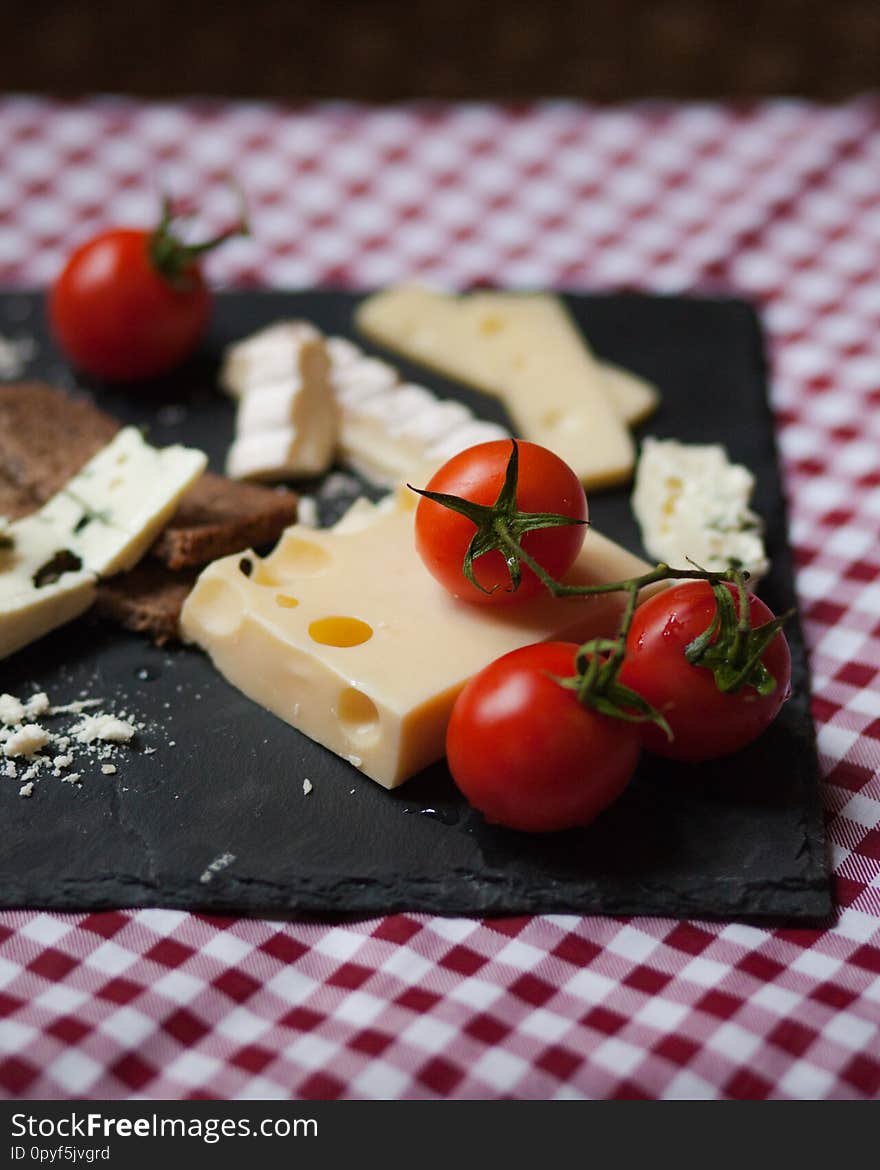 Delicious plate of french cheese served with fresh ripe tomatoes and bread on a black charcoal board. Red and white tablecloth for a picnic mood. Delicious plate of french cheese served with fresh ripe tomatoes and bread on a black charcoal board. Red and white tablecloth for a picnic mood