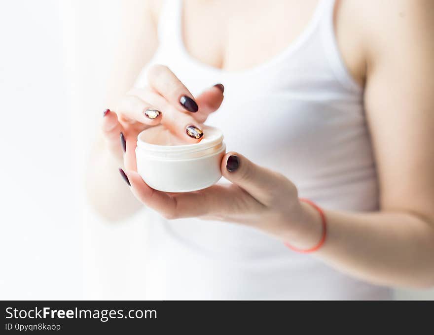 A beautiful blonde woman holds a jar of cream in her hand and applies it to her body. Skin care by moisturizing