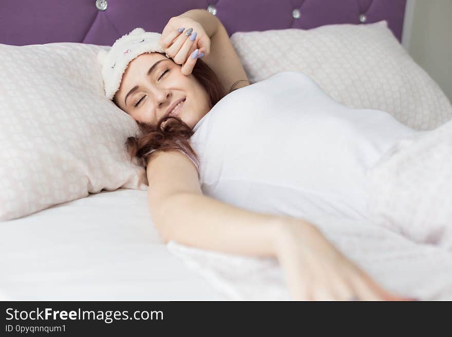 An attractive young brunette girl woman wakes up in her bed in a sleep mask.