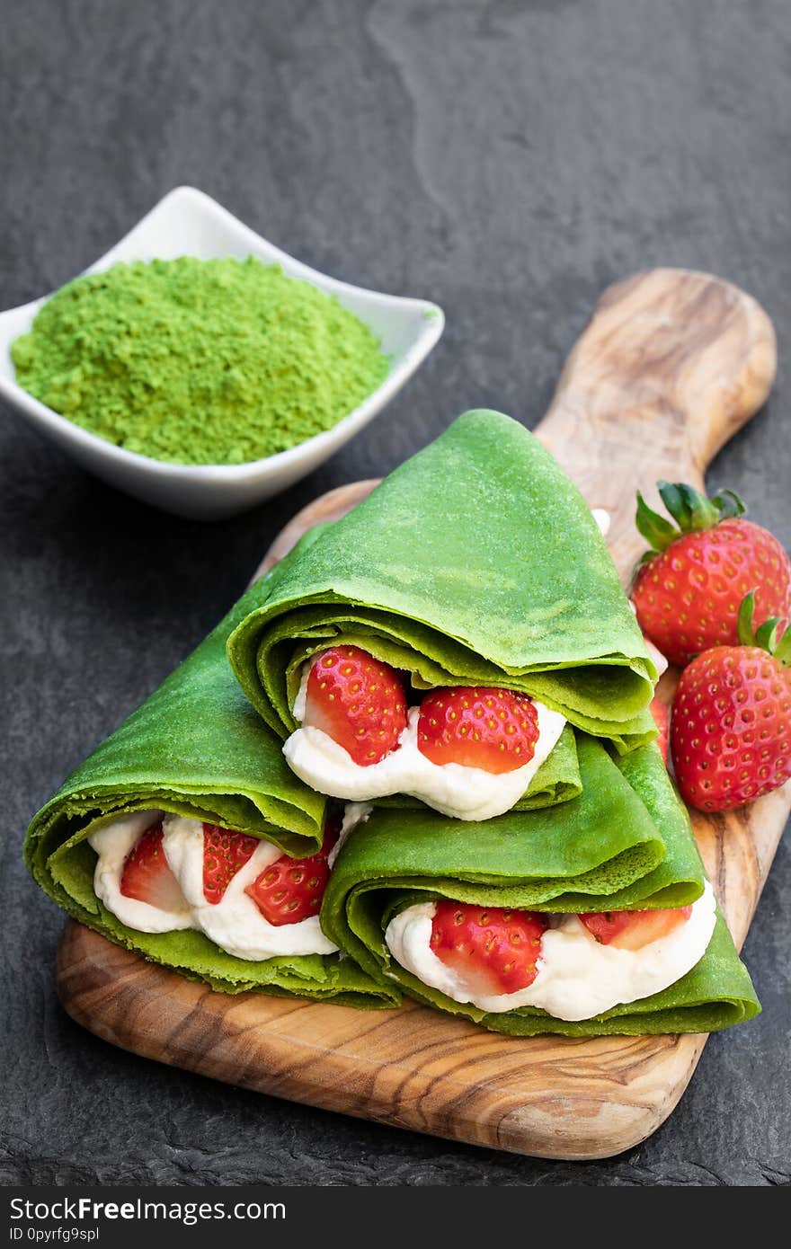 Matcha green tea crepe with whipped cream and strawberry on serving board