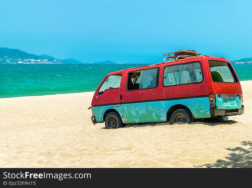 Old red bus in sand of beach with blue sea background