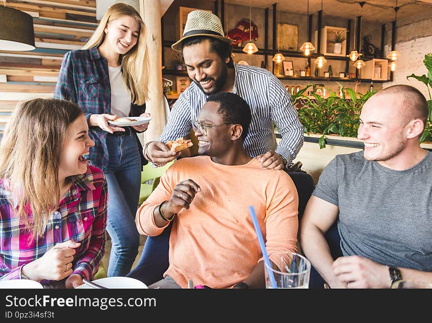 A company of multicultural  young people in a cafe eating pizza, drinking cocktails, having fun.