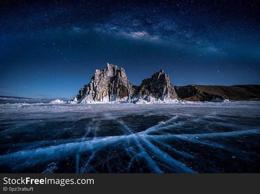 Landscape of Shamanka rock and milky way on sky with natural breaking ice in frozen water on Lake Baikal, Siberia, Russia.