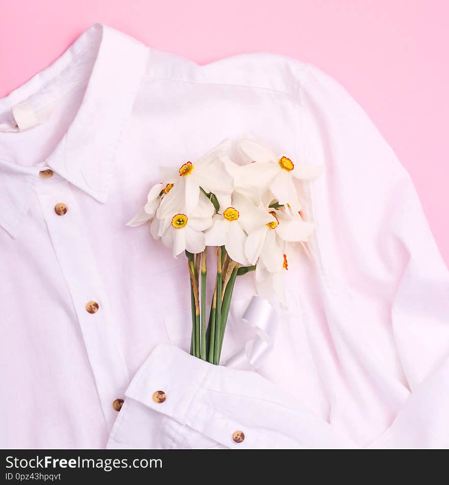 Delicate spring bouquet of white daffodils on a white basic shirt on a pink background. Top view, flat lay. Delicate spring bouquet of white daffodils on a white basic shirt on a pink background. Top view, flat lay