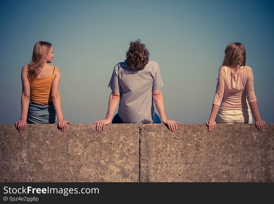 Happiness summer friendship concept. Group of friends spending time together having fun outdoor sitting on wall against blue sky