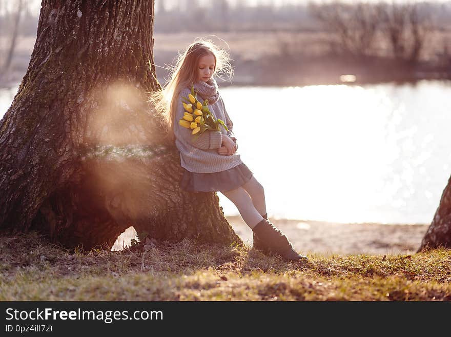A girl with yellow tulips in early spring on a cold windy evening near the river