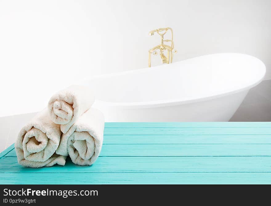 Blue wooden shelf with rolled towels on bathroom background. Wood desk table with top view and copy space near white bath at hotel. Room service and shower spa concept. Selective focus